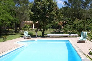 Une piscine avec deux chaises longues, entourée d’arbres et avec un bâtiment en arrière-plan.
