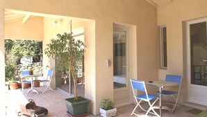 An outdoor patio area with a table and chairs, potted plants, and a sliding glass door leading to a balcony. - Quiet cottage near Carcassonne pool (Ventenac-Cabardès)