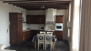 A compact kitchen with wooden cabinets, a microwave, an oven, and a dining area with a table and chairs. - Apartment hyper center of Saint Omer (Saint-Omer)