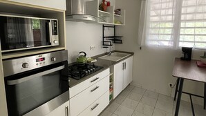 Een moderne keuken met een ingebouwde magnetron, oven en gasfornuis. Er is een raam met gordijnen, een hangende lamp en een aanrecht met een waterkoker.
