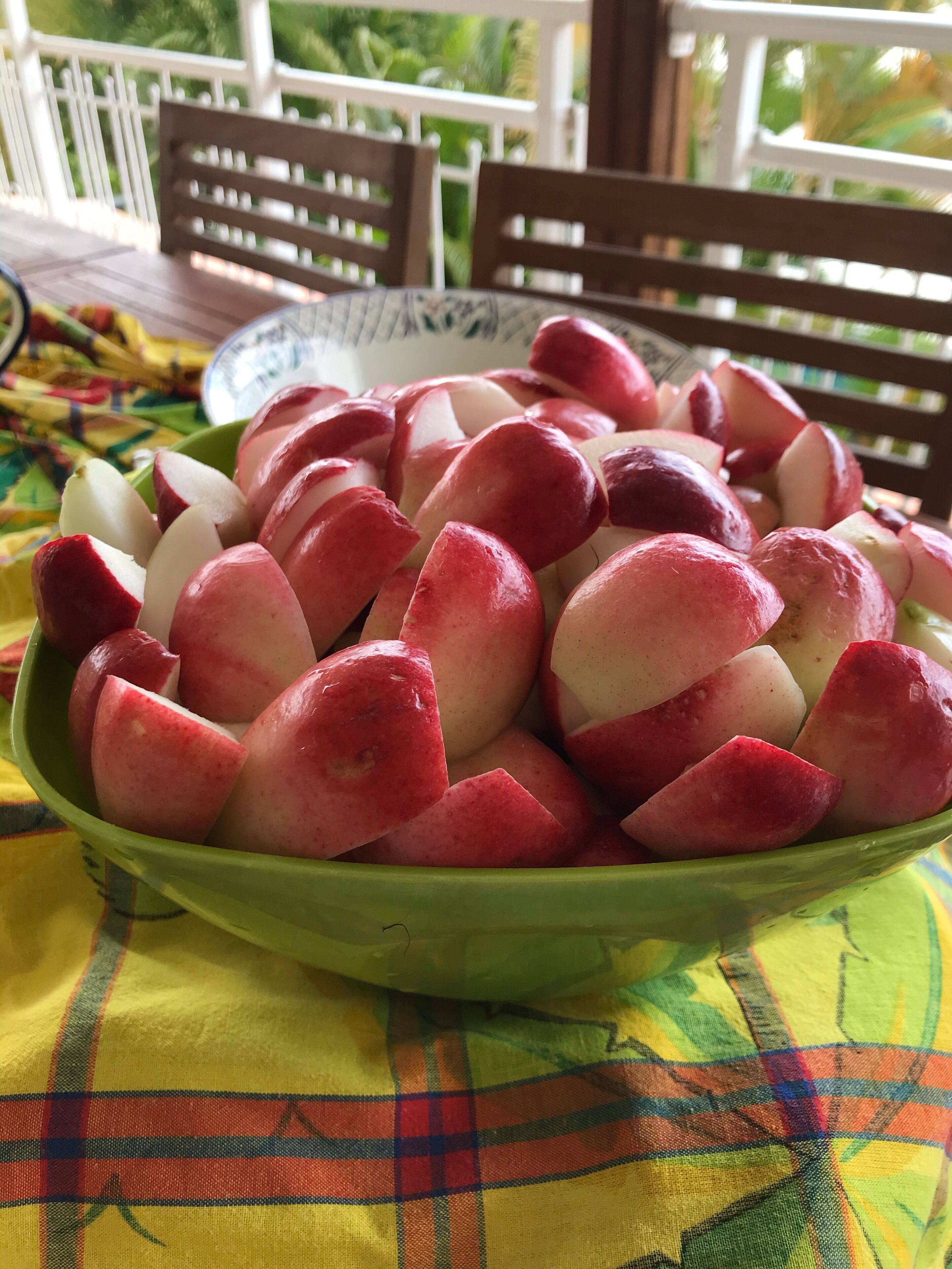 A bowl of sliced red and white apples on a table with a colorful tablecloth.