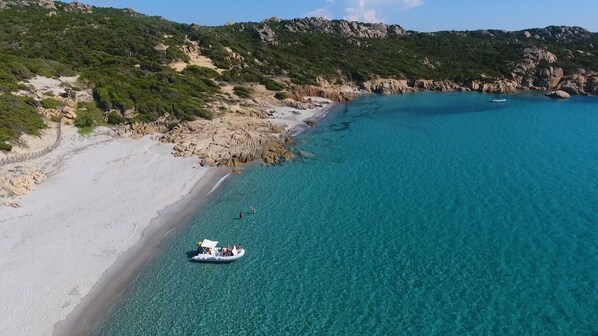 A coastal beach with clear turquoise waters, rocky terrain, and a boat near the shore.
