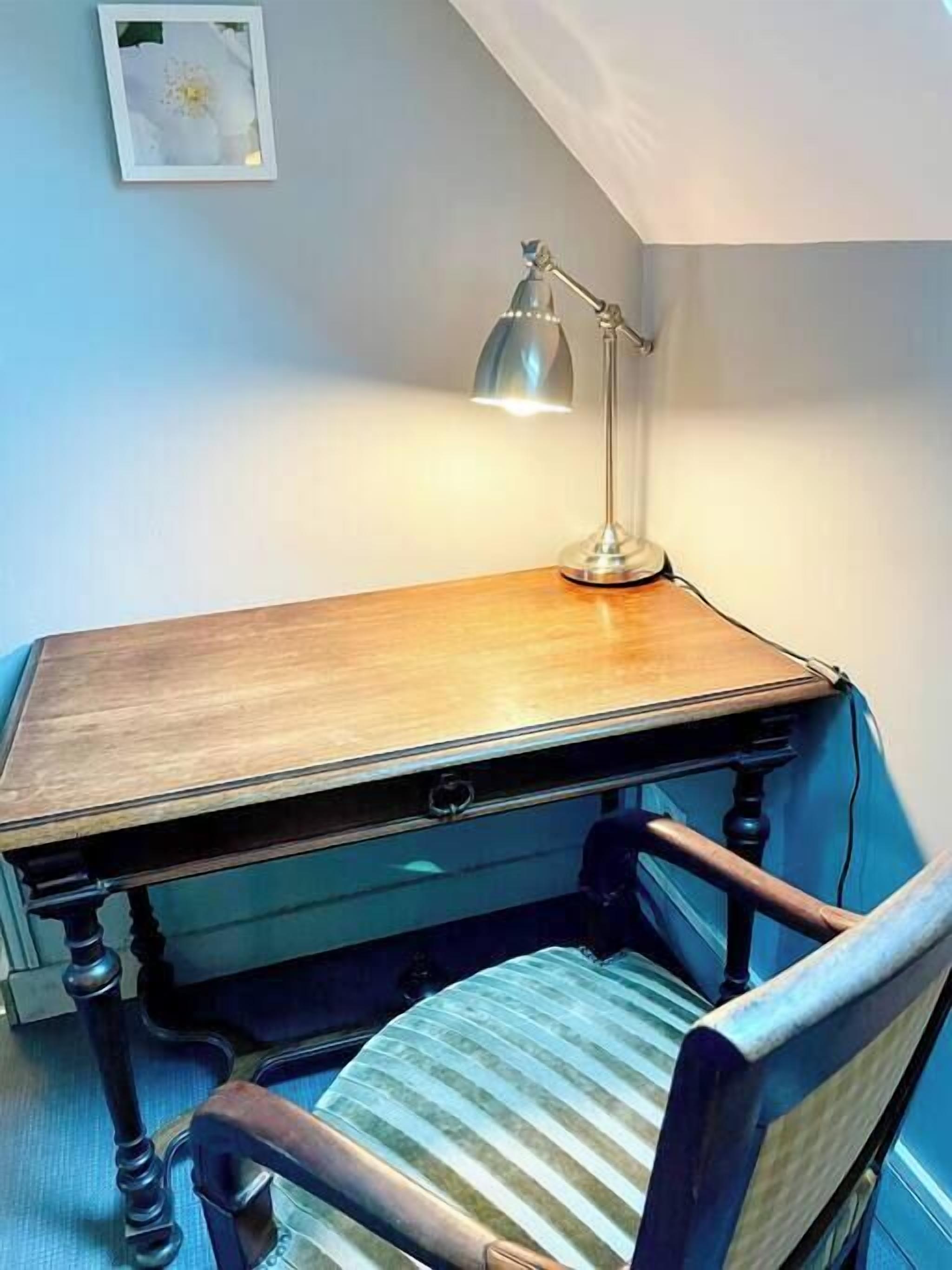 Ett skrivbord i trä med en låda, en lampa och en stol med ett randigt sittdyn.