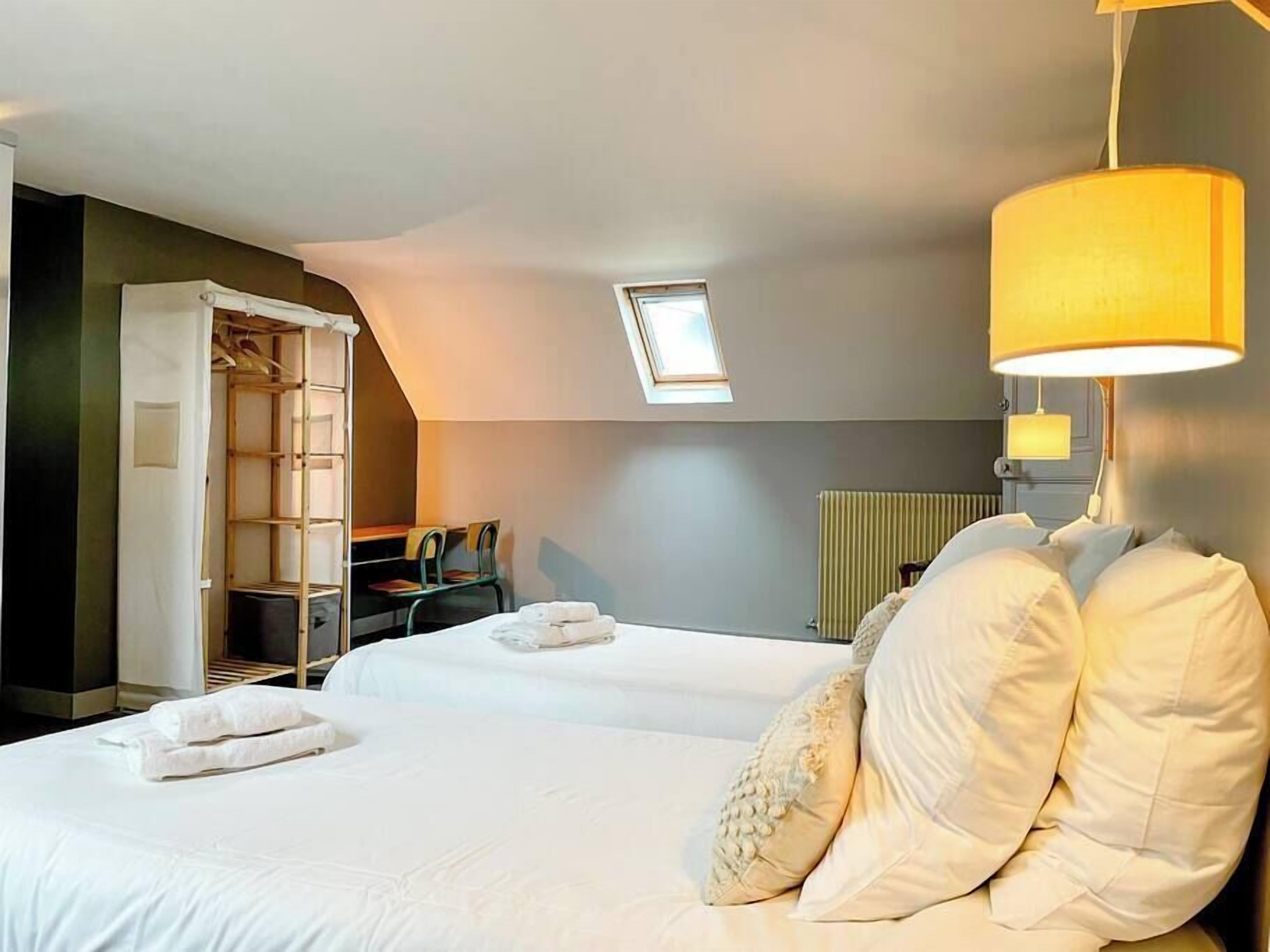 A hotel room with two beds, a skylight, a desk with chairs, and a radiator.