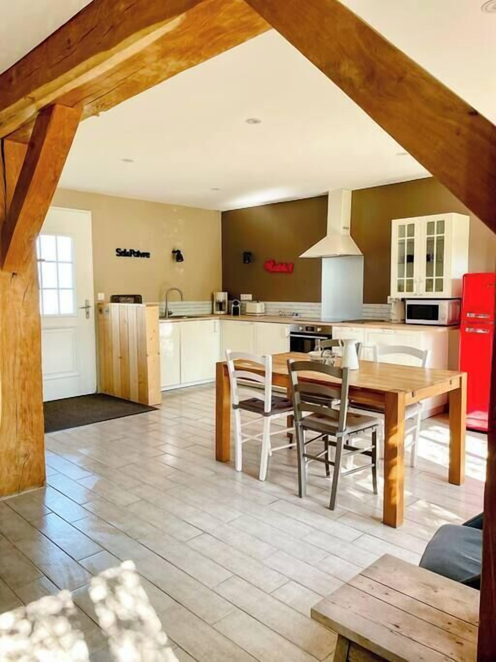 Une cuisine moderne avec des poutres en bois, un coin repas avec une table et des chaises en bois, et un réfrigérateur rouge.