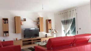 Un salón con televisor de pantalla plana, sofás rojos, estanterías de madera y una mesa de centro de vidrio.
