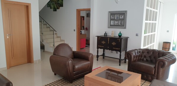 Una sala de estar con un sofá de cuero marrón, una mesa de centro de vidrio y un aparador de madera oscura con objetos decorativos.