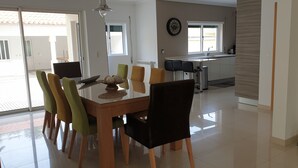 Un comedor con mesa y sillas de vidrio, una cocina al fondo y vista al exterior.
