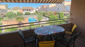 A balcony with a table and chairs, overlooking a swimming pool and residential buildings. - Spacious and pleasant T3 with pool near beach, port, leisure island  (Agde)