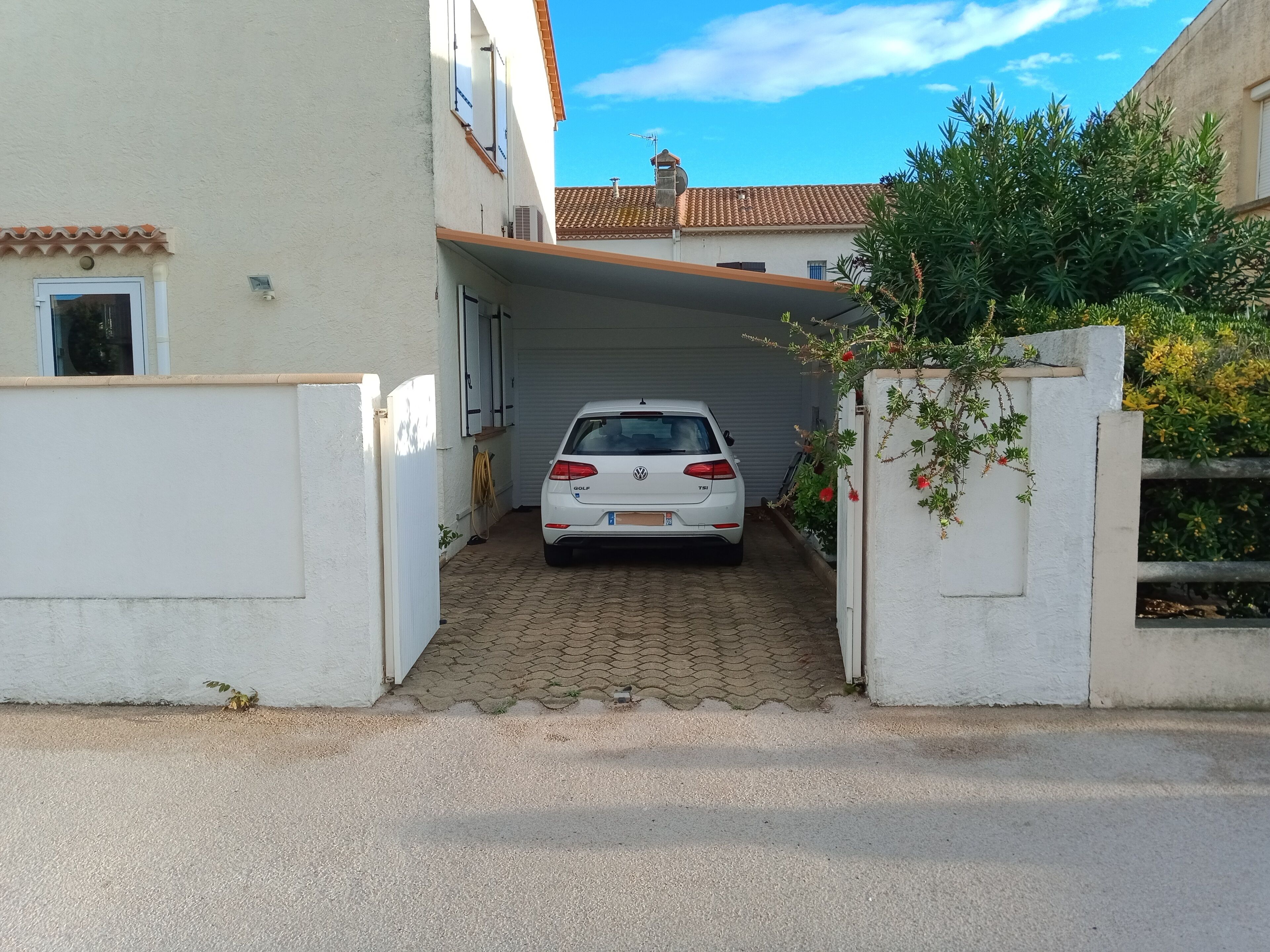 A white car parked in a driveway leading to a house with a tiled roof and a covered garage.