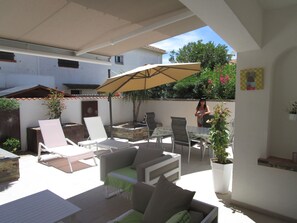 Un patio al aire libre con una mesa, sillas y un sofá bajo un paraguas grande.