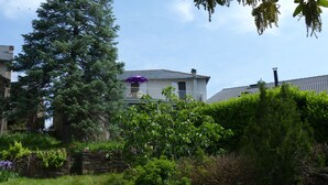 Een huis met balkon, omringd door groen en een grote boom.
