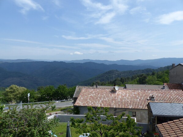 A residential area with terracotta-tiled roofs, surrounded by lush greenery and distant mountains.