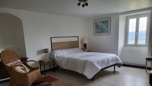Een slaapkamer met een bed, een stoel, een nachtkastje, een lamp en een raam met uitzicht.