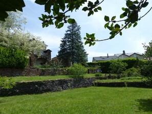 A stone wall, a grassy lawn, and a large tree in a garden setting.