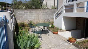 Un patio con una mesa y sillas, rodeado de plantas en macetas y un muro de piedra.