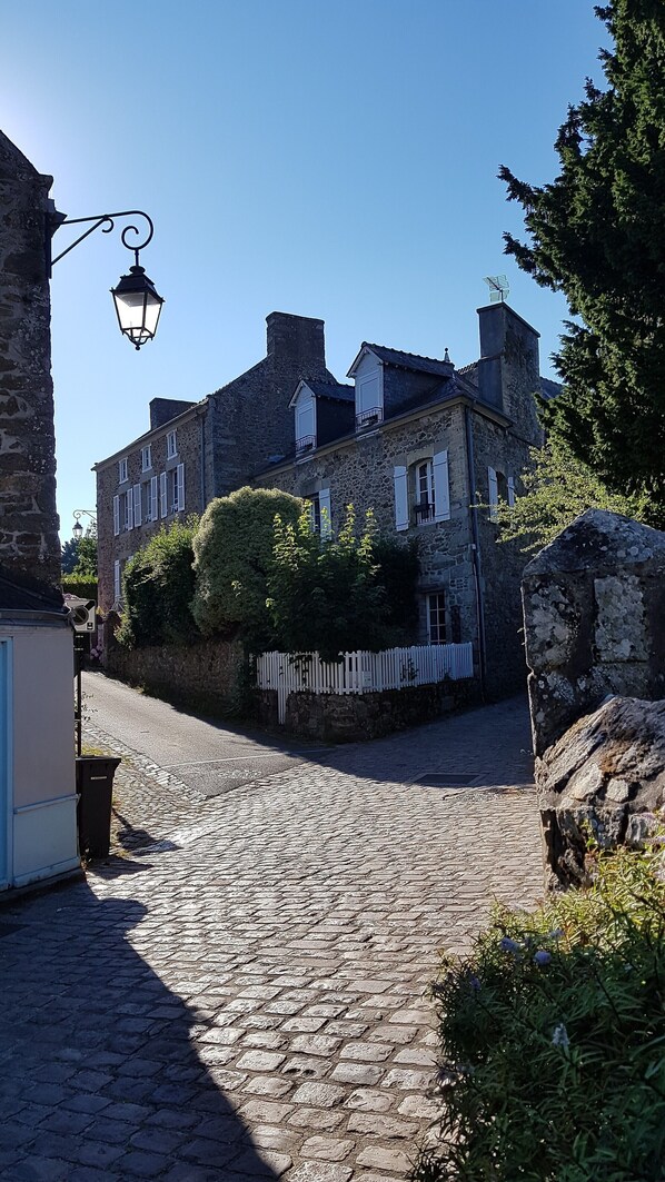 A cobblestone street leading to a stone building with multiple windows and a white picket fence.