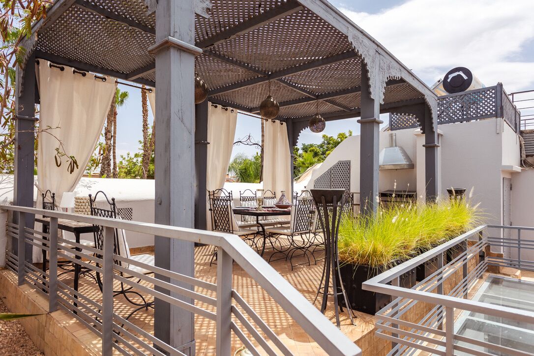 An outdoor patio area with a pergola, tables, chairs, and a grill.