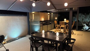 Un área de comedor al aire libre con mesa y sillas, una parrilla y una carpa encima.