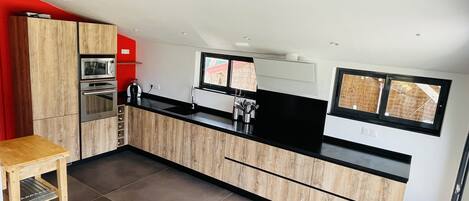 A modern kitchen with wooden cabinets, a black countertop, and a window with a view.