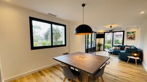 Ein moderner Wohnraum mit Essbereich, einer Sofagarnitur und einem großen Fenster mit Blick auf Grünflächen.