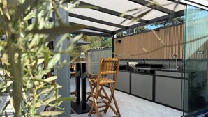 Eine moderne Außenküche mit Holzstuhl, Tisch und Glastrennwand.