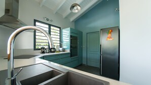 A modern kitchen with teal cabinetry, a stainless steel sink, and a refrigerator with a cartoon character magnet.