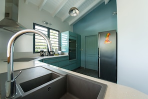 A modern kitchen with teal cabinetry, a stainless steel sink, and a refrigerator with a cartoon character magnet.
