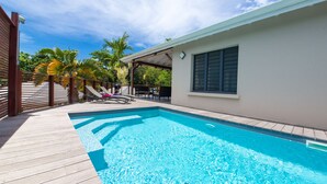 A swimming pool with a wooden deck, lounge chairs, and palm trees in the background.