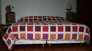 Quarto com cama grande, piso de madeira, duas mesas de cabeceira com luminárias e um guarda-roupa.