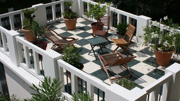 Terraço no telhado com piso xadrez, móveis de madeira e plantas em vasos.