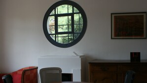Uma sala de jantar com uma mesa redonda, cadeiras, uma janela com padrão quadriculado, um eletrodoméstico branco e um armário de madeira.