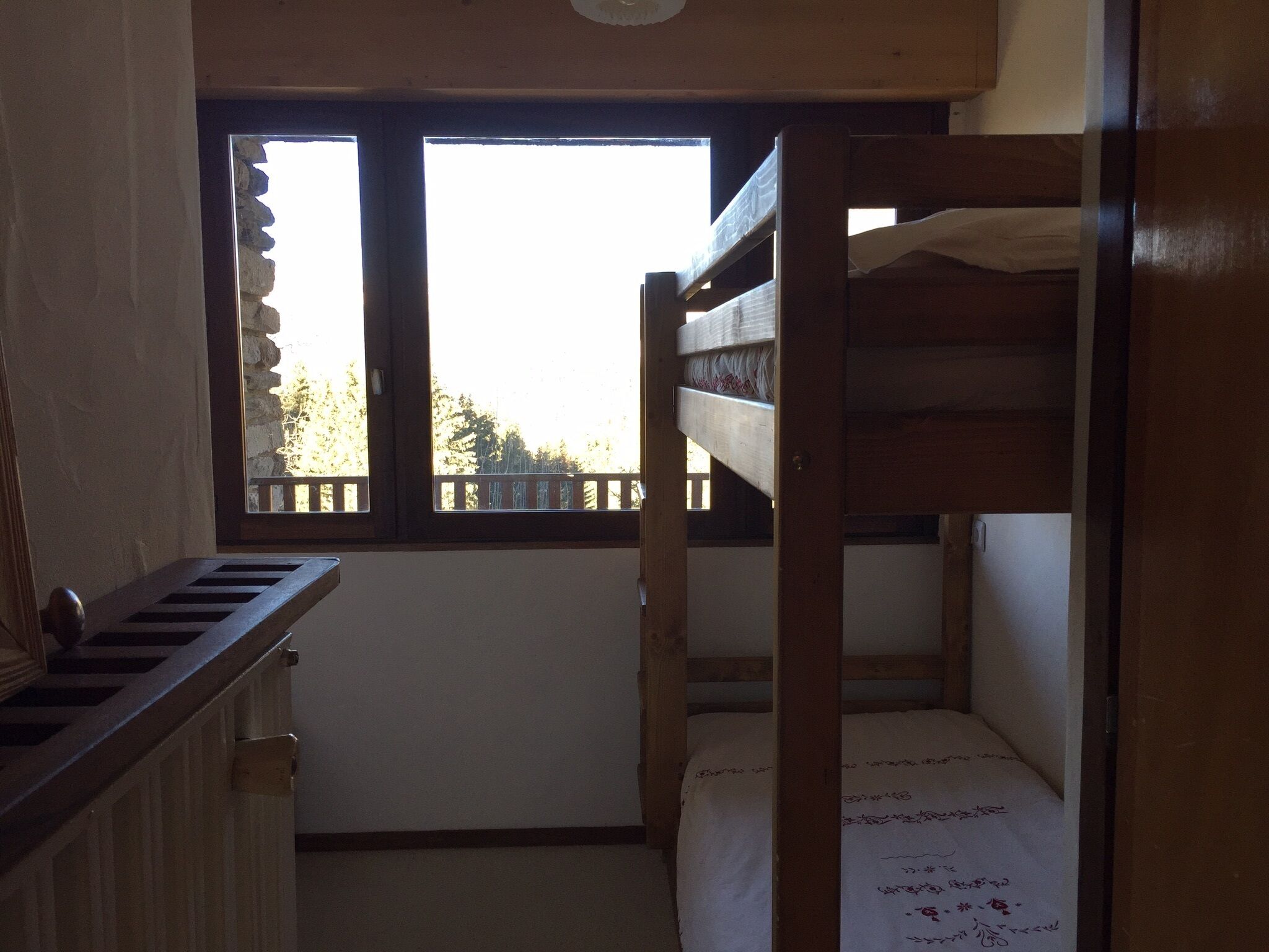 A bunk bed room with a window, wooden walls, and a small bench.