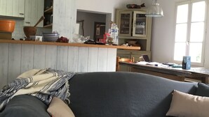 Ein gemütlicher Wohnbereich mit einem dunkelgrauen Sofa, einem Holztisch und einer Küche im Hintergrund.