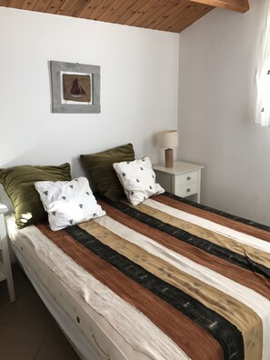 A neatly made bed with striped bedding, two pillows, a bedside lamp, and a framed picture on the wall.