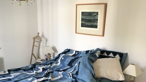 Ein Schlafzimmer mit Bett, Nachttisch, Lampe, einer Leiter und einem gerahmten Bild an der Wand.
