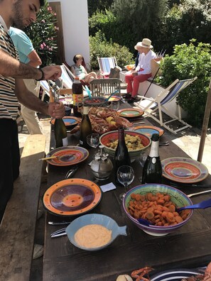 Mesa de comedor al aire libre con diferentes platos, bebidas y una botella de vino.