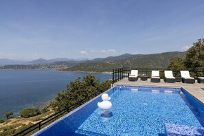 A swimming pool with lounge chairs and a view of the sea and mountains.