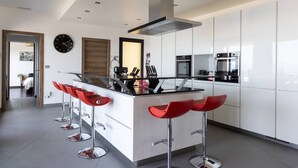 Une cuisine moderne avec des meubles blancs, un îlot central doté de tabourets de bar rouges, des appareils en acier inoxydable et un éclairage encastré au plafond.
