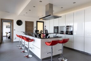 Une cuisine moderne avec des meubles blancs, un îlot central doté de tabourets de bar rouges, des appareils en acier inoxydable et un éclairage encastré au plafond.