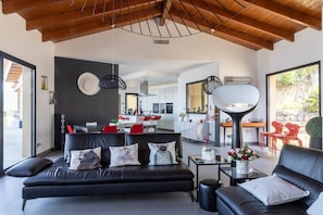 A modern living room with a black sofa, a coffee table, and a dining area with red chairs.