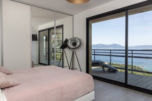 A bedroom with a large bed, a mirror, and a view of the sea.