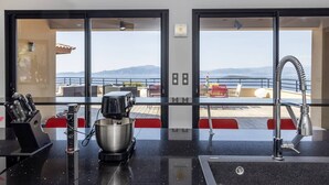 Une cuisine équipée d’une machine à café, d’un évier et offrant une vue sur la mer grâce à de grandes fenêtres.