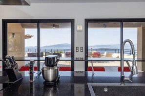 A kitchen with a coffee machine, a sink, and a view of the sea through large windows.