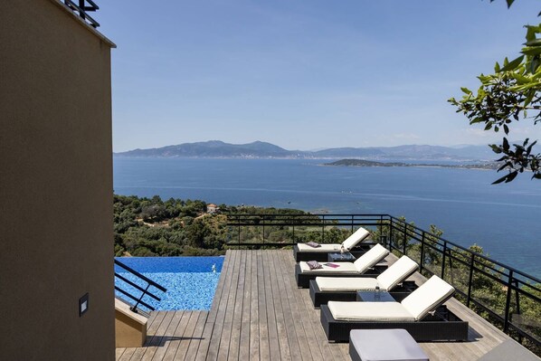 A deck with lounge chairs overlooking a pool and a sea view.