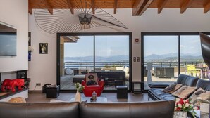 A modern living room with a large window, a red chair, a black sofa, and a wooden ceiling.