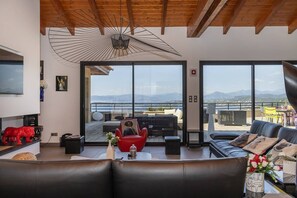 A modern living room with a large window, a red chair, a black sofa, and a wooden ceiling.