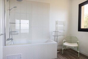 Ein Badezimmer mit einer gläsernen Duschkabine, einer weißen Badewanne, einem grünen Stuhl und einem weißen Handtuchhalter.