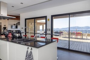 Eine moderne Küche mit einer großen Kochinsel, ein Essbereich mit Outdoor-Möbeln und Blick auf das Meer.