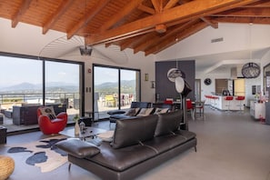 A spacious living area with a leather sofa, red chair, and a large window overlooking mountains.